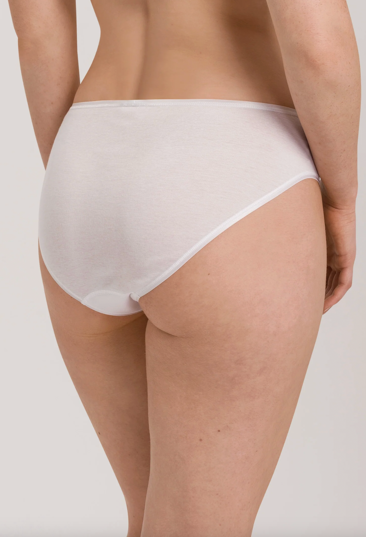 Rear view of a model wearing white high-waisted briefs against a light gray studio background.