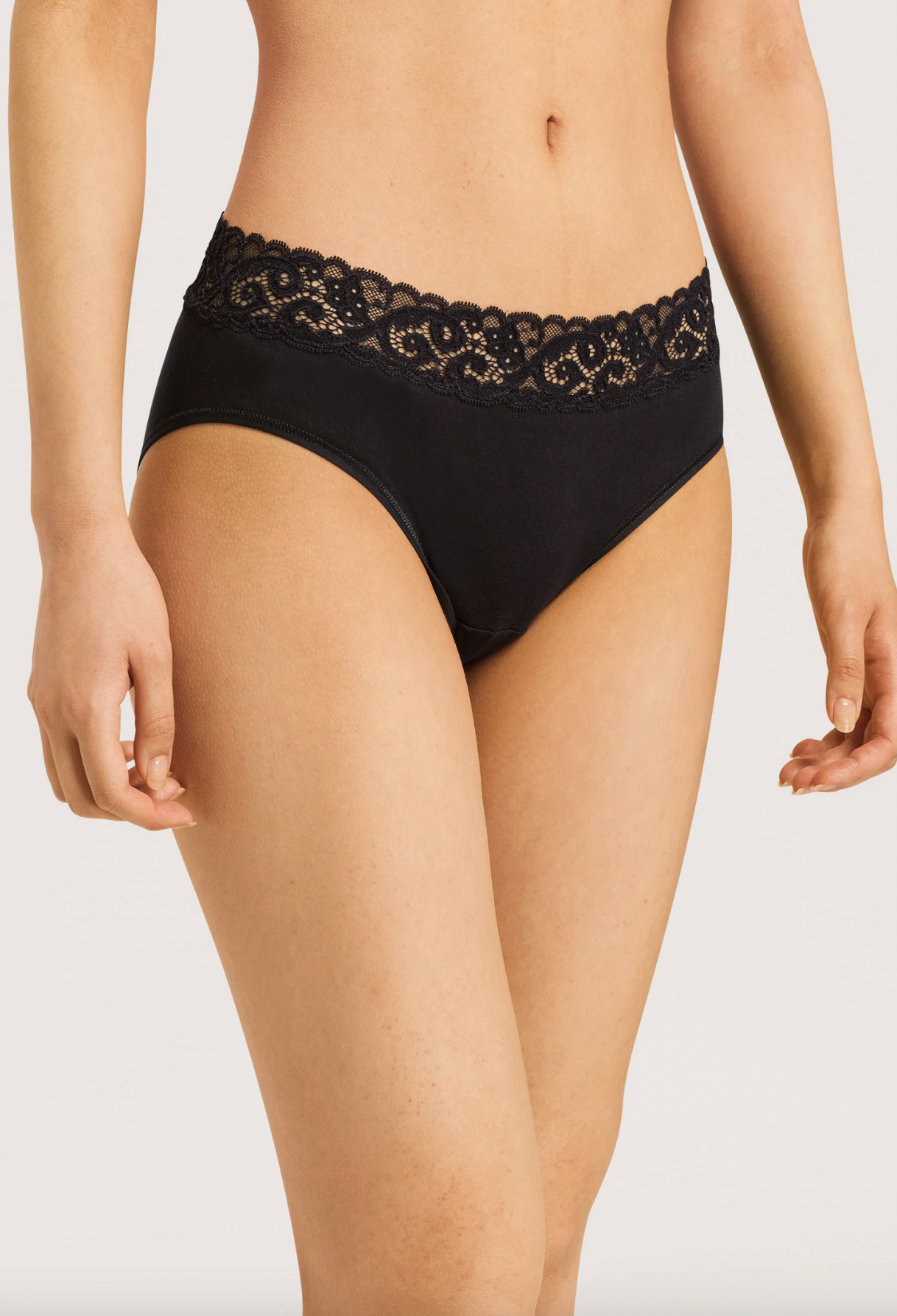 Black lace-trimmed underwear worn by a model, shown from the waist to upper thighs against a light gray studio background.