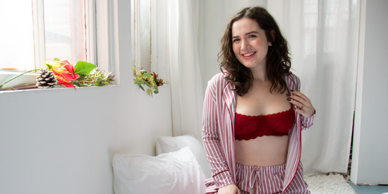 Woman wearing a red bra and striped shirt in a bright room with white curtains and flowers.