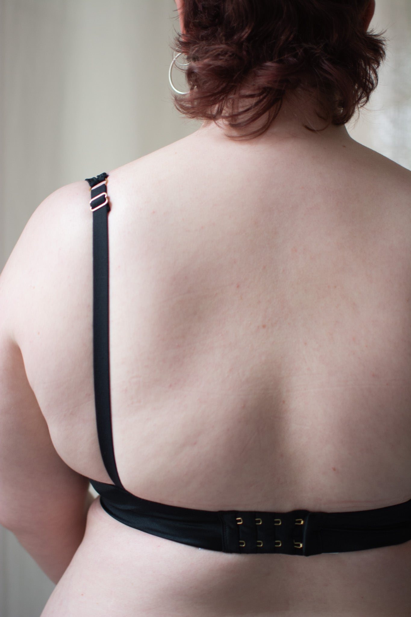 Person wearing black lace bra on neutral background.