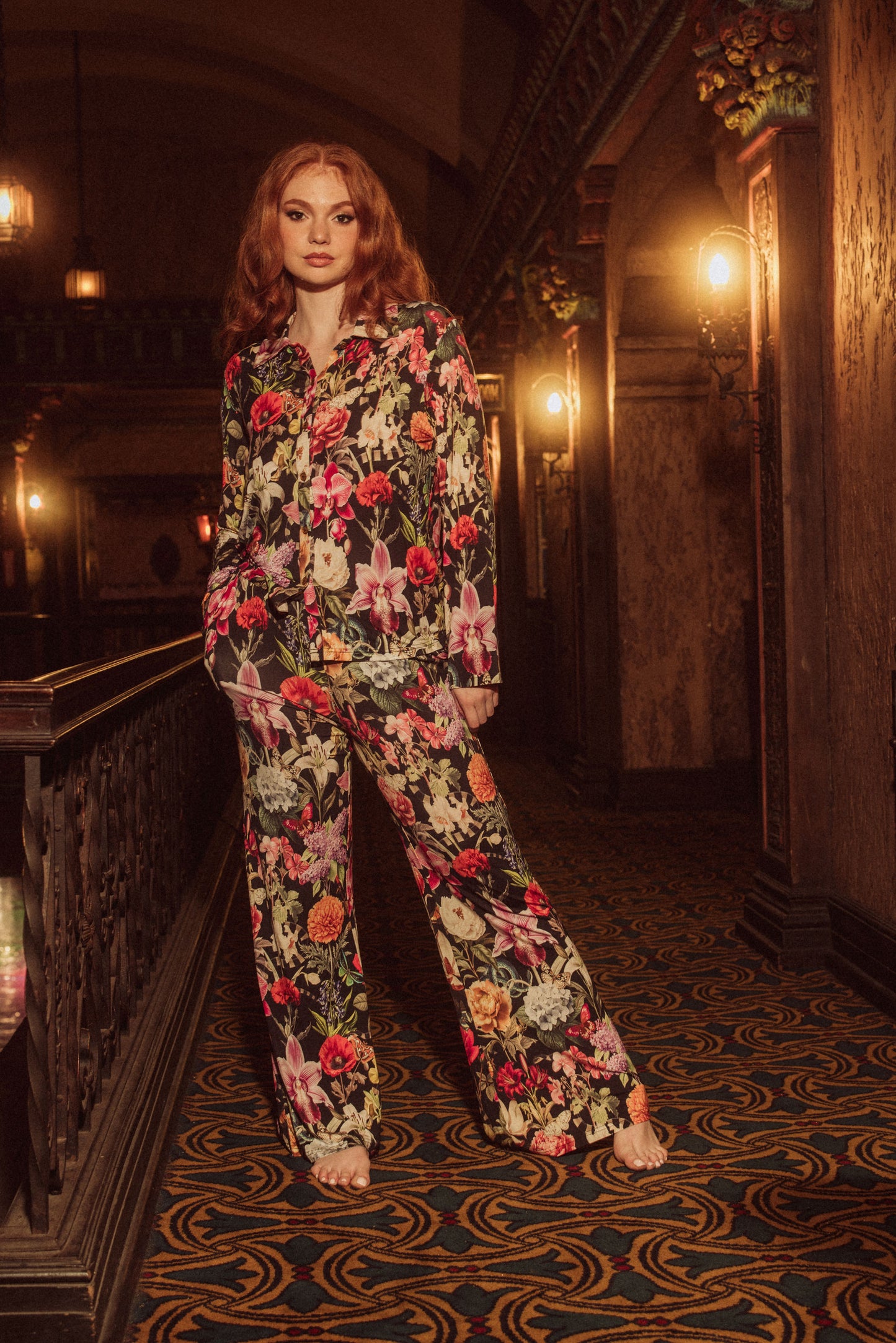Woman in a floral pajama set standing in an ornate hallway.