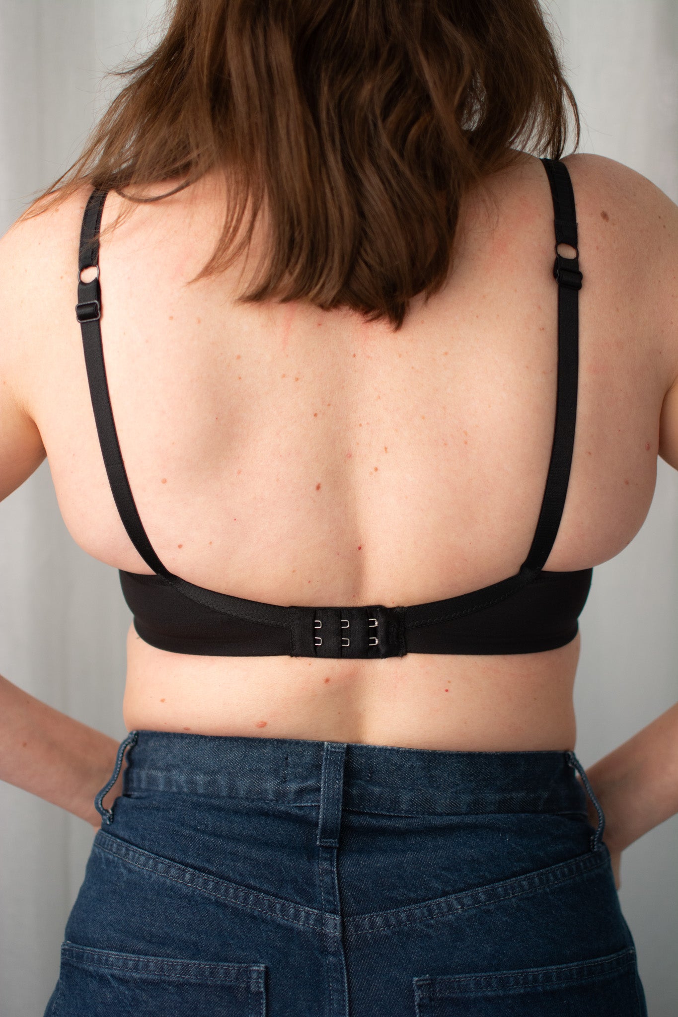 Person wearing a black bra and dark blue jeans against a neutral background