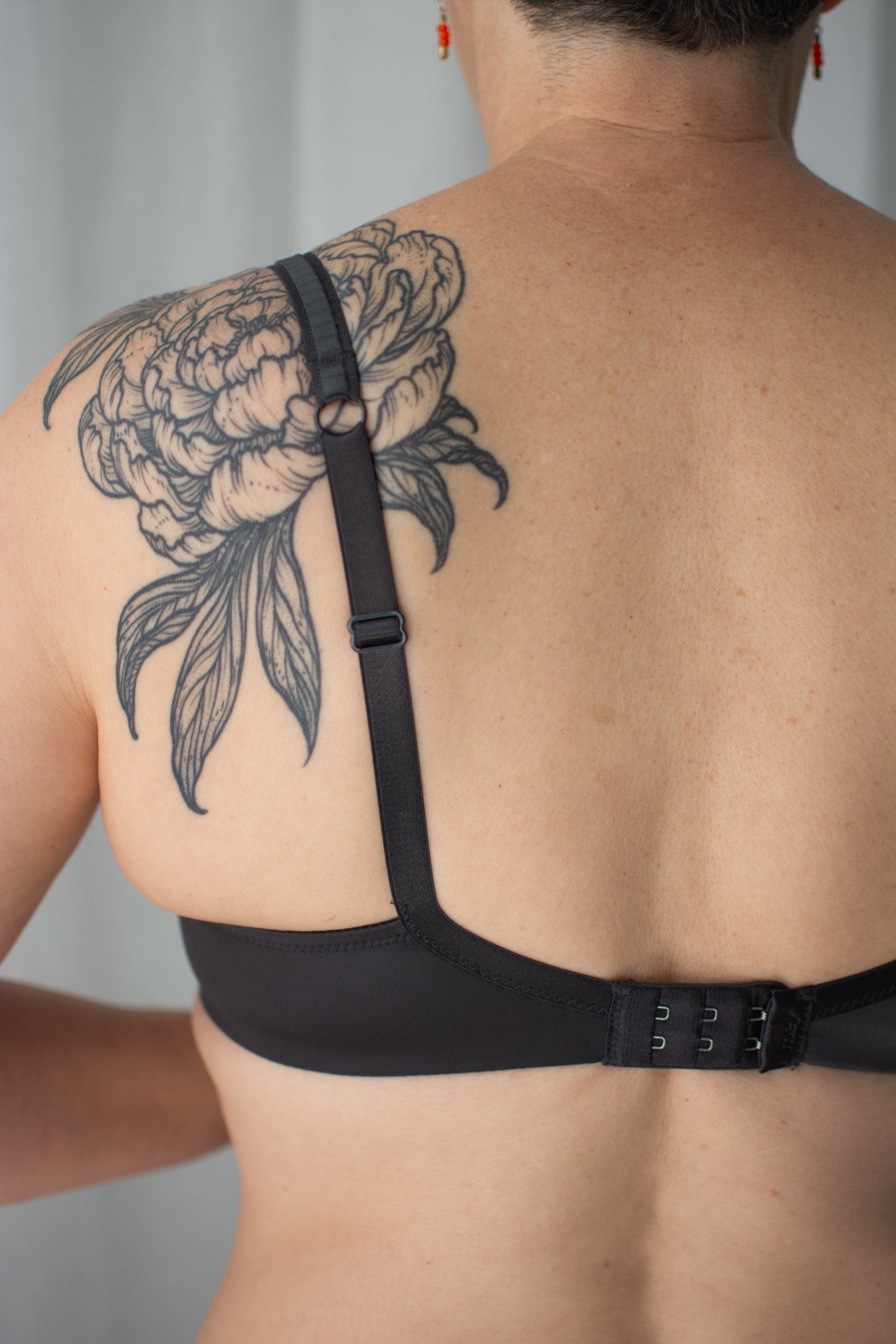 Person wearing a black bra with a large tattoo on their shoulder blade against a neutral background
