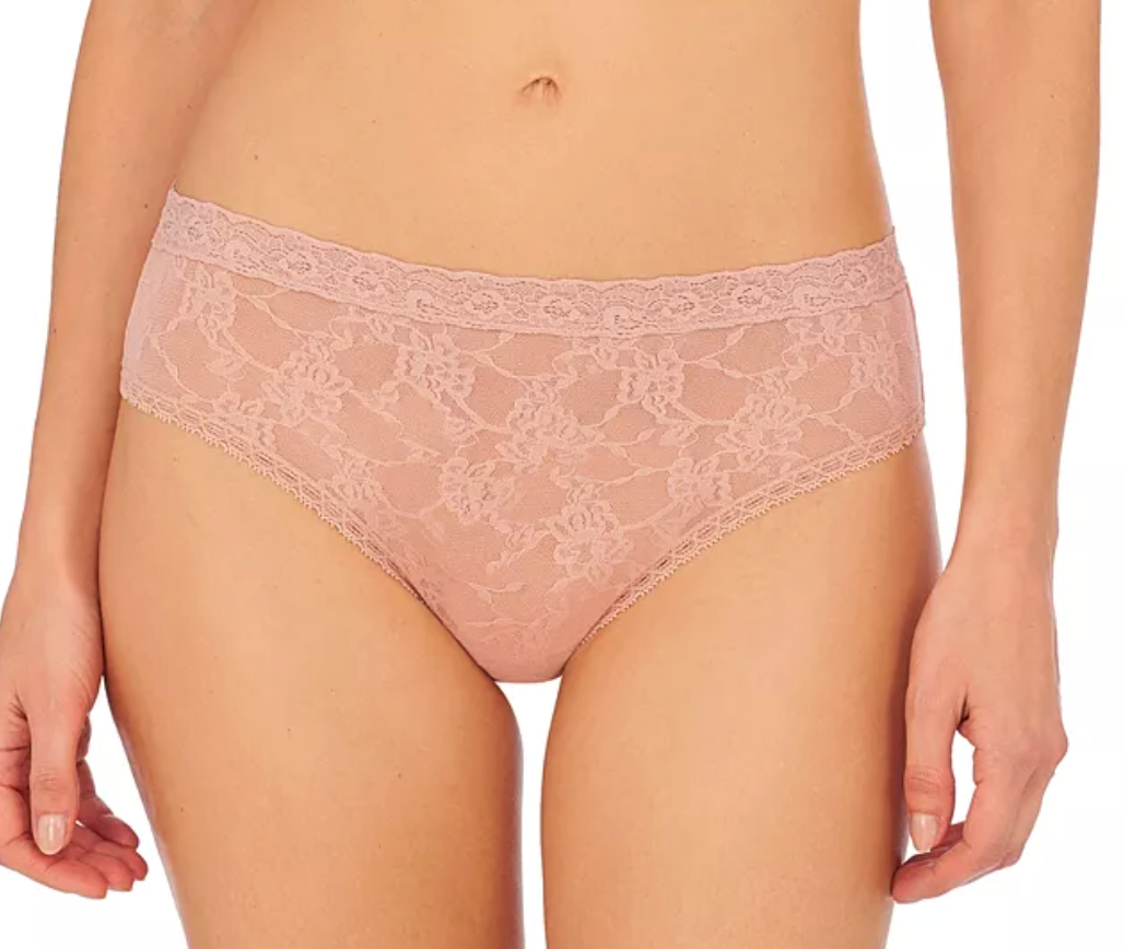 A close-up of a model wearing light pink lace underwear against a plain white background.
