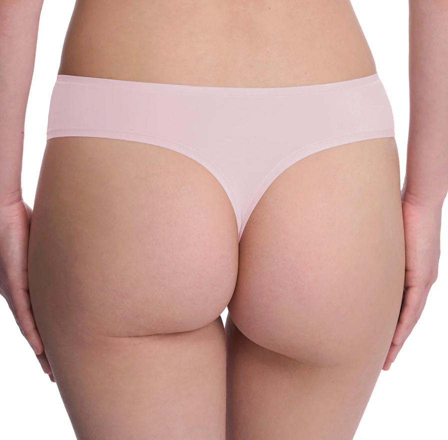 Rear view of a model wearing a light pink seamless thong against a white background.