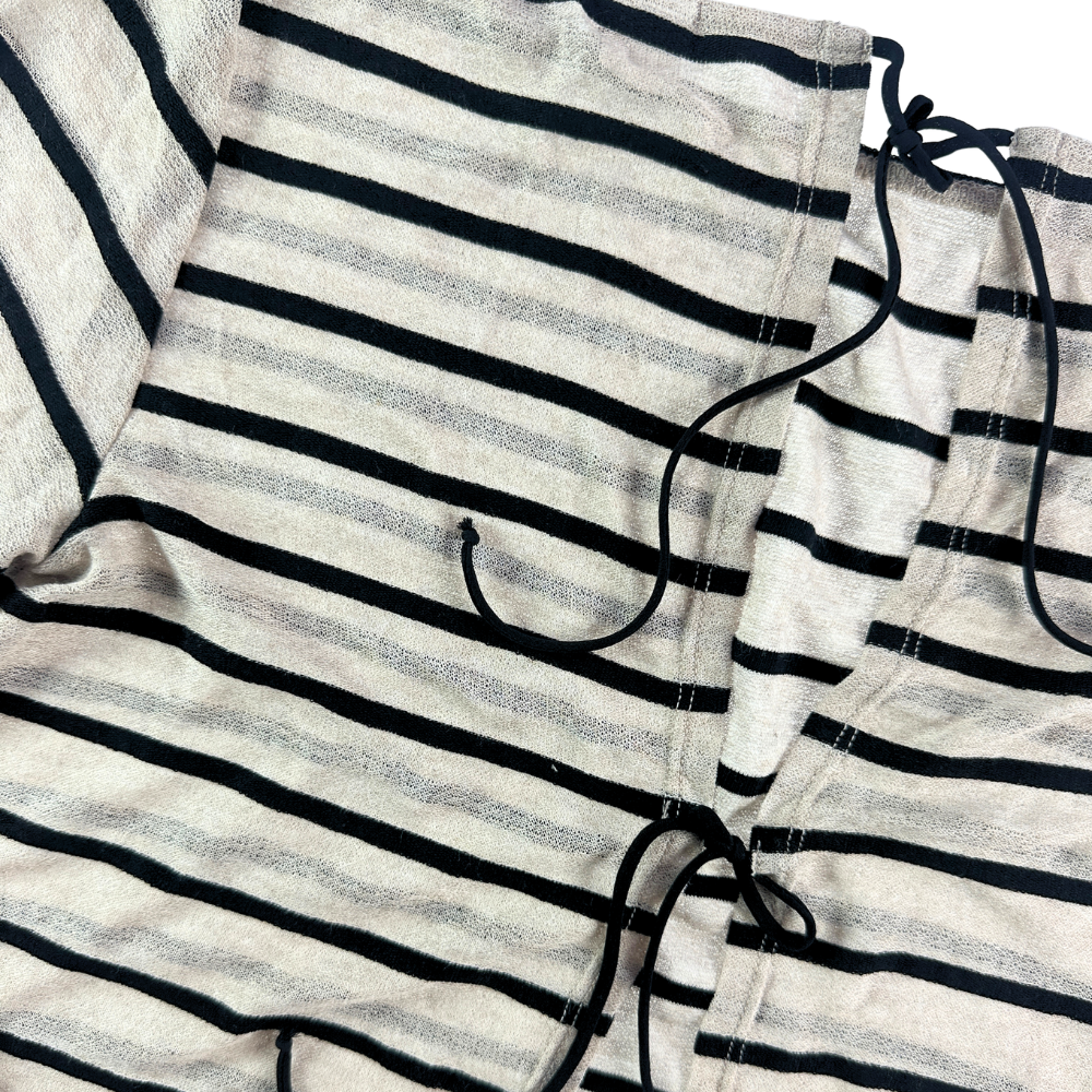 Close-up of a striped knit garment, likely a top or dress, with horizontal black and off-white stripes and black drawstrings visible at the neckline and waist.
