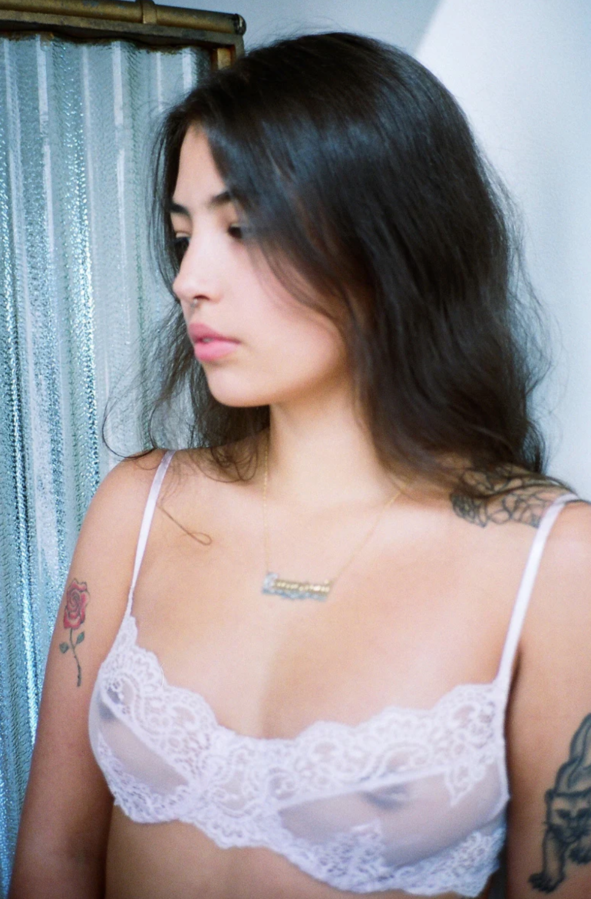 Model wearing white lace bra in a room infont of a curtain.