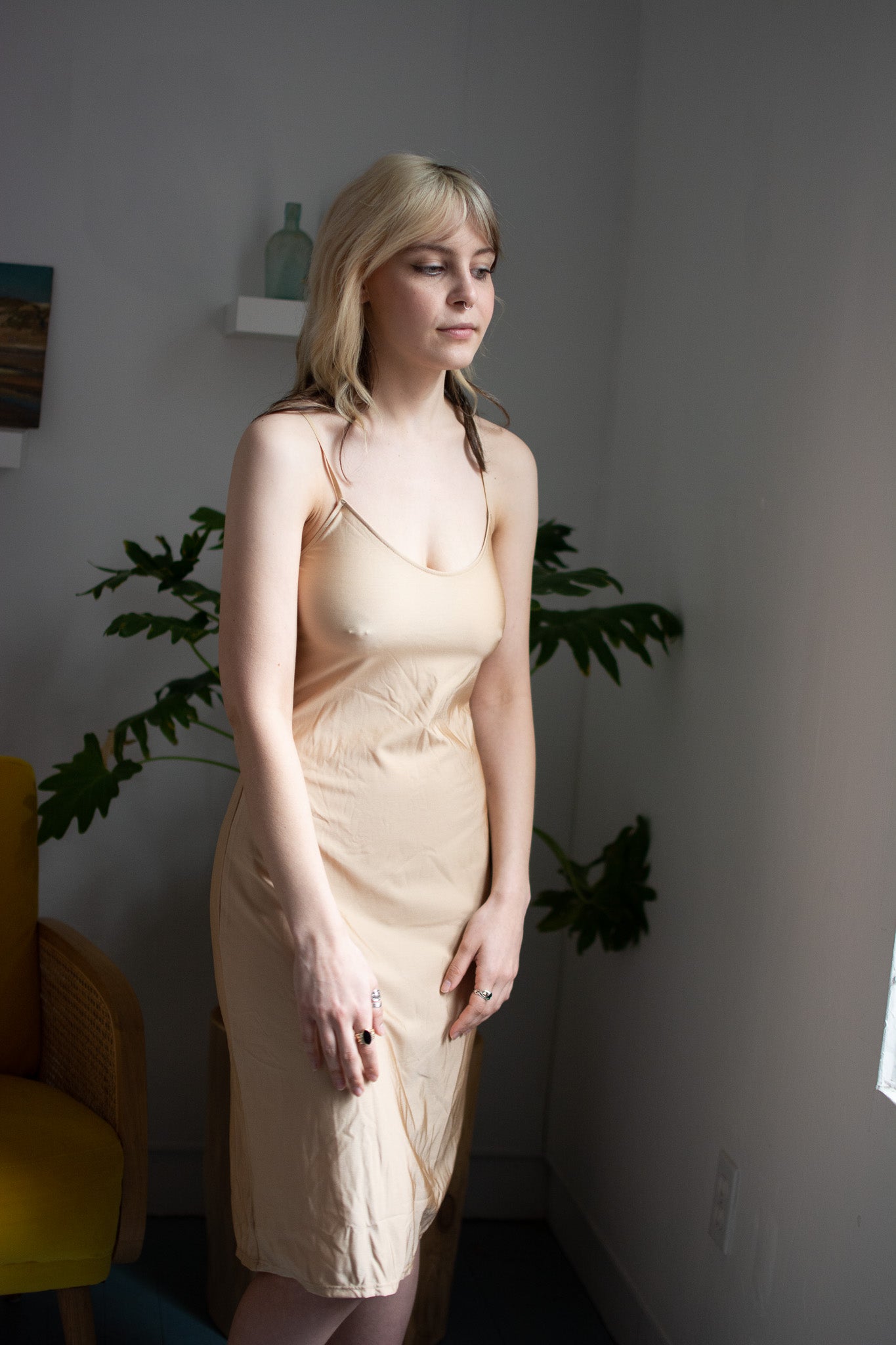 Woman wearing a beige slip dress in a room with plants and a yellow chair.
