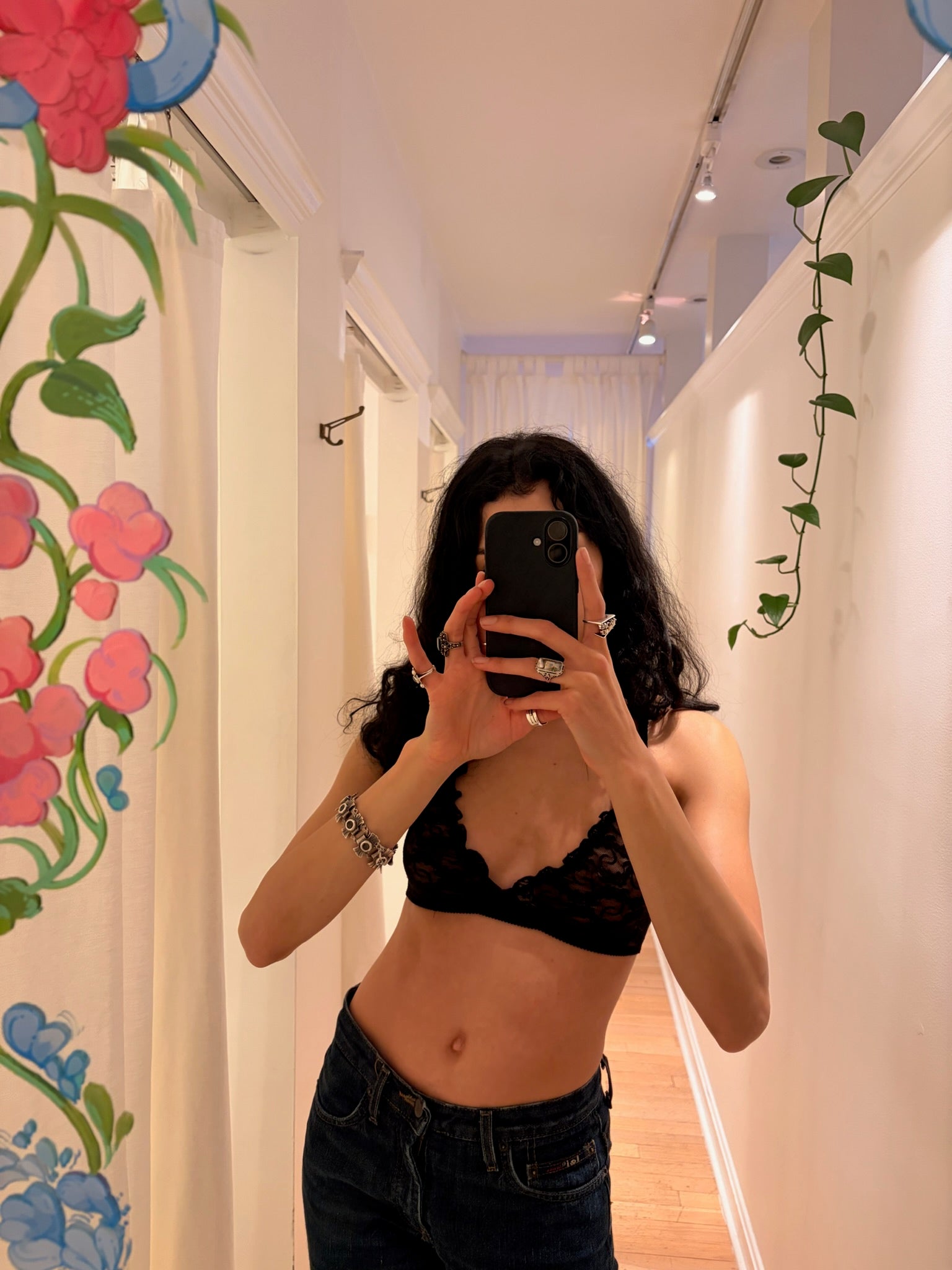 Person taking a mirror selfie in a room with floral decorations.