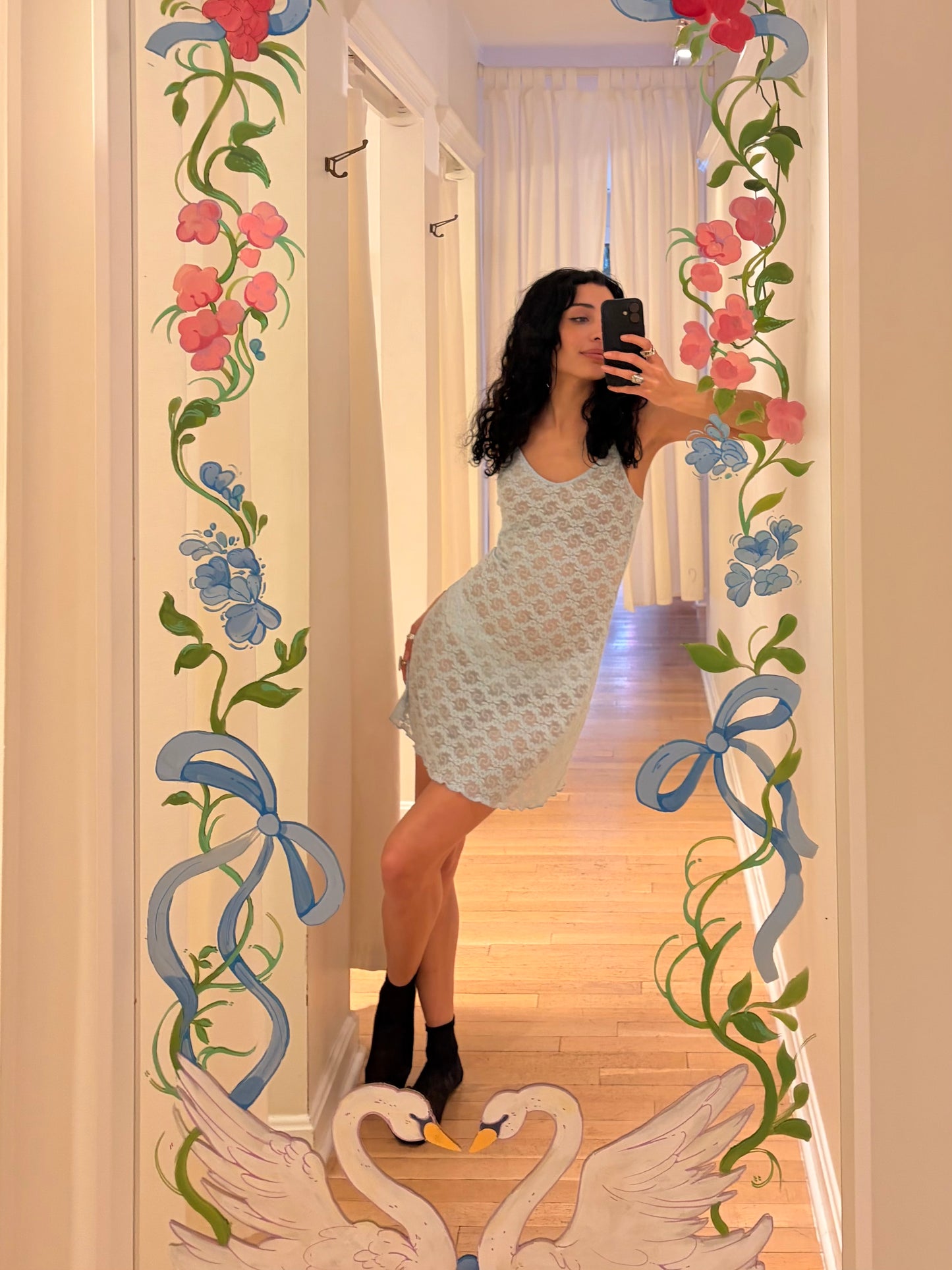Person taking a mirror selfie with decorative floral and swan designs on the frame.