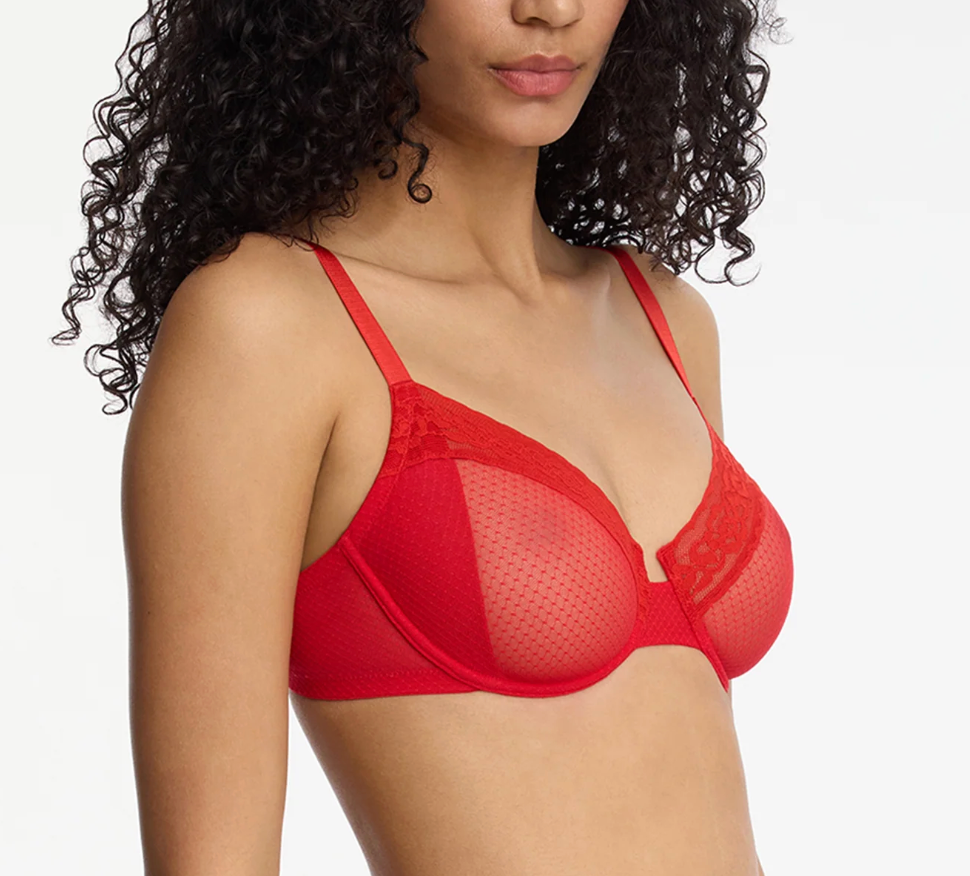 A close-up of a model wearing a bright red seamless underwire bra with sheer mesh cups and lace trim, set against a plain light gray background.