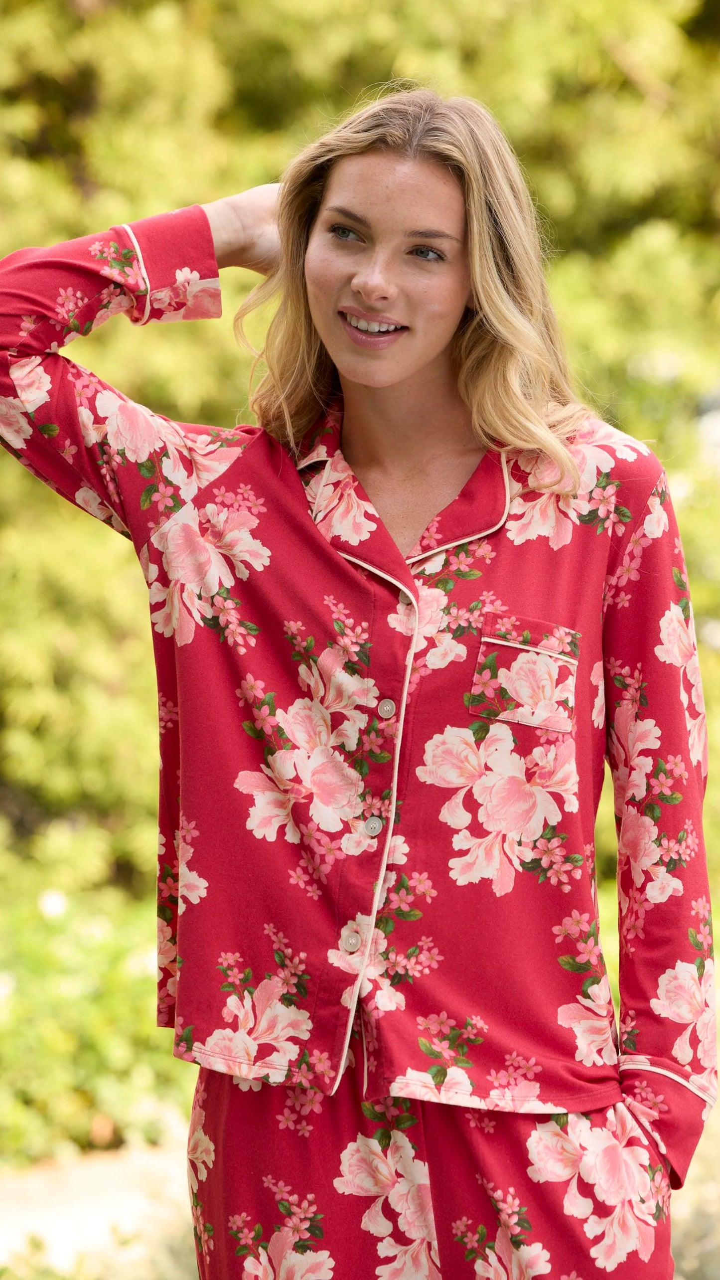 model wearing red floral long pajamas outside against some greenery.
