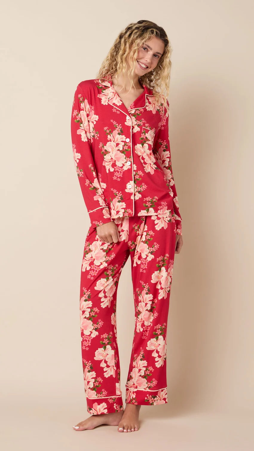 model wearing long red pajamas with floral print against a white background. 