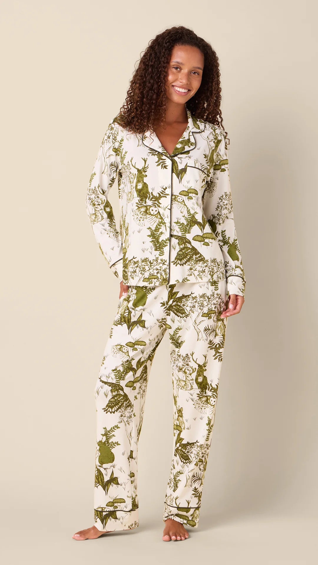 model wearing white long pajamas with green animal and floral printed on them against a neutral background