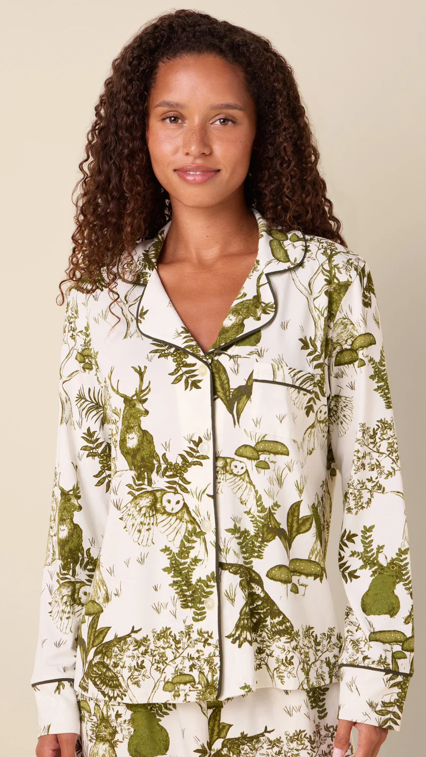 model wearing white long pajamas with green animal and floral printed on them against a neutral background