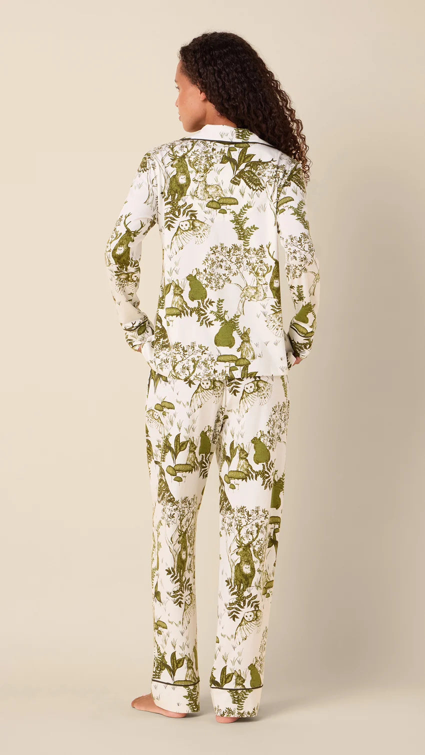 back of model wearing white long pajamas with green animal and floral printed on them against a neutral background