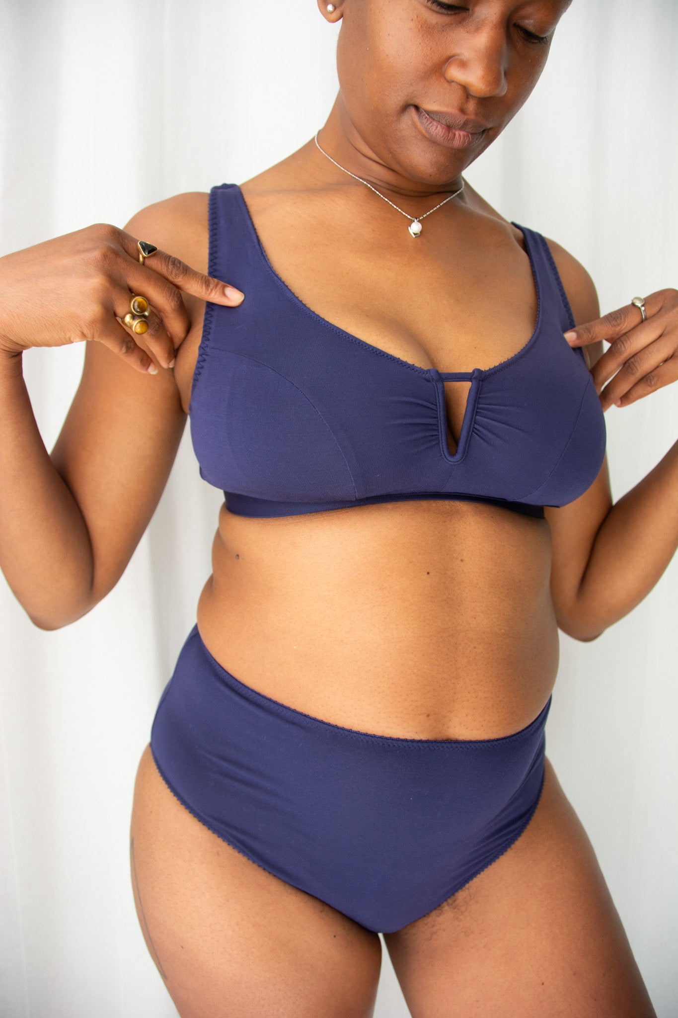 Woman wearing a navy bra and underwear against a white curtain background