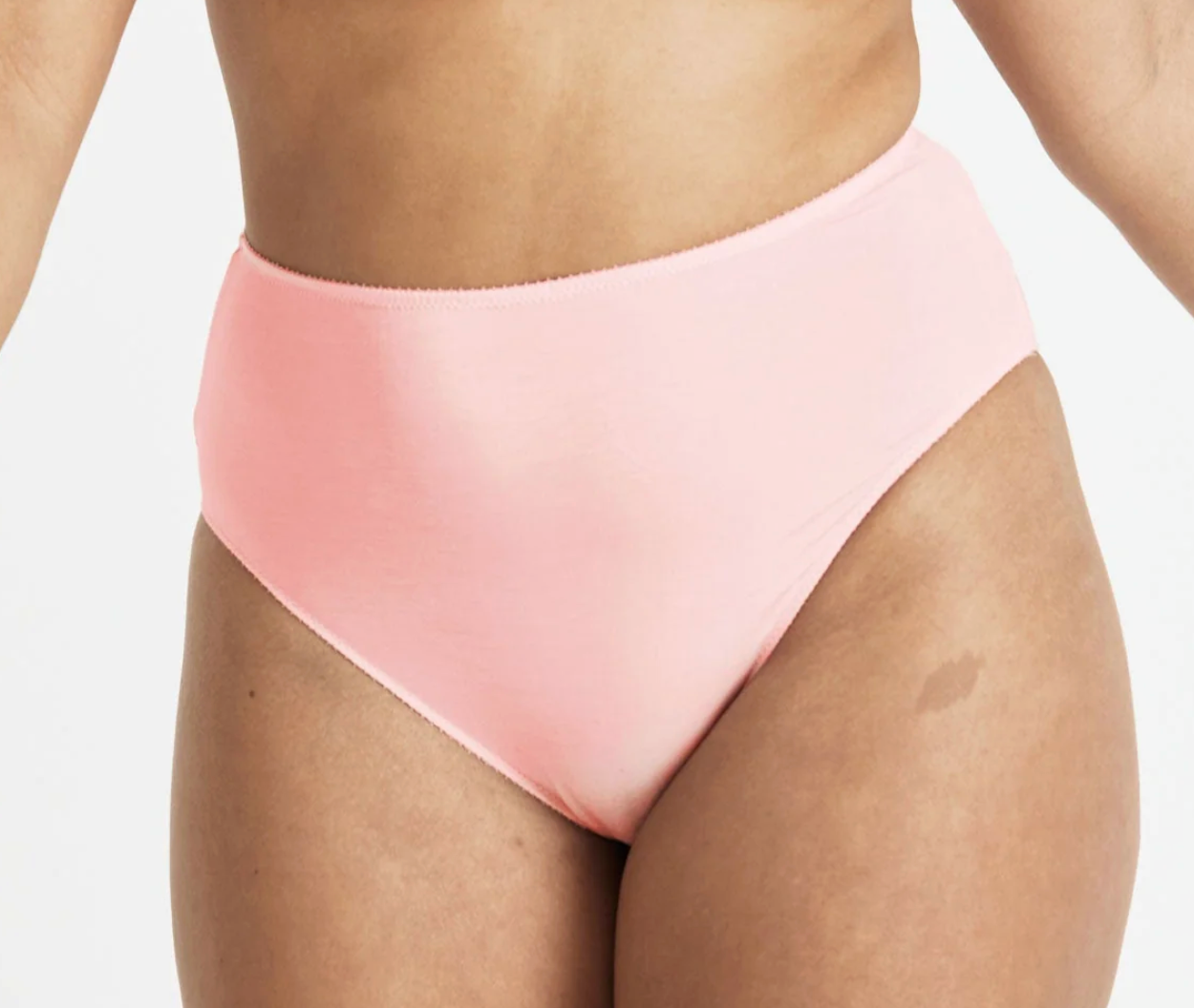A close-up of a model wearing high-waisted, solid light pink bikini bottoms against a clean white background.