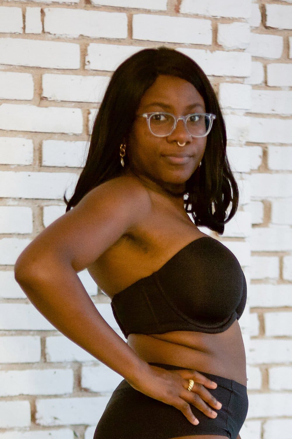 Wacoal red carpet strapless bra in black, front-side view on a model against a brick wall.