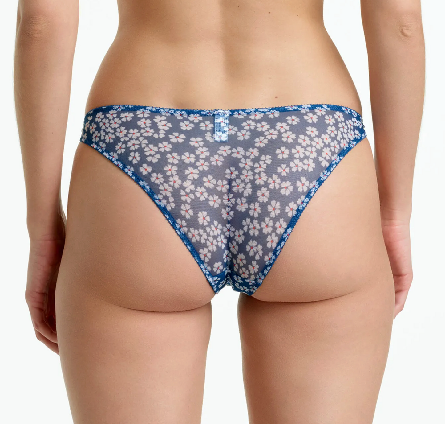 Rear view of a model wearing sheer blue mesh thong underwear with a white floral print and blue trim, shown against a plain white background.