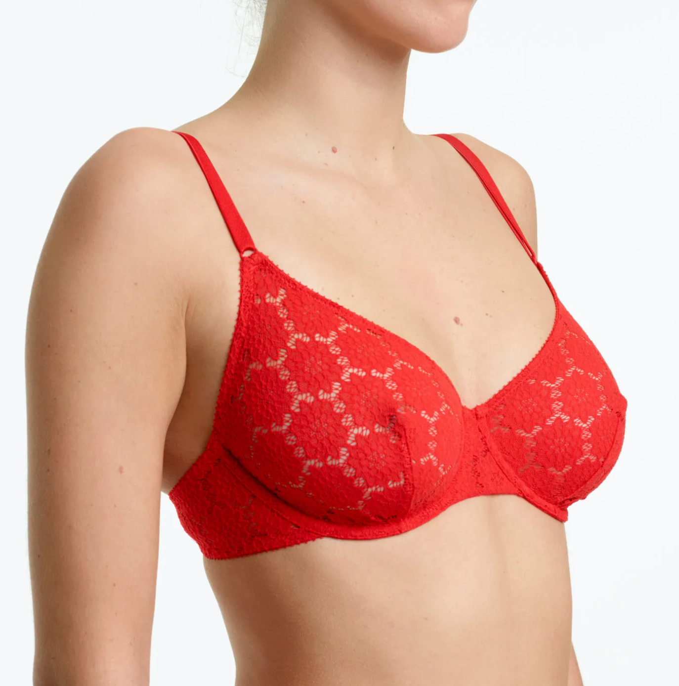 A close-up of a model wearing a bright red lace bra with thin straps and a repeating geometric floral pattern.