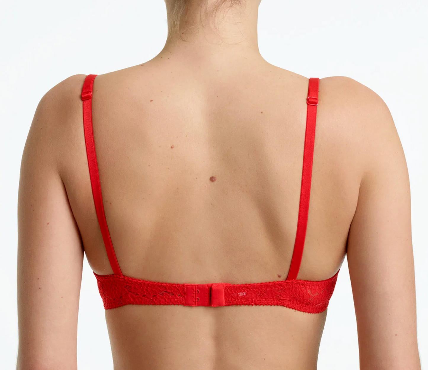 Rear view of a woman wearing a bright red lace bra with thin adjustable straps against a plain white background.