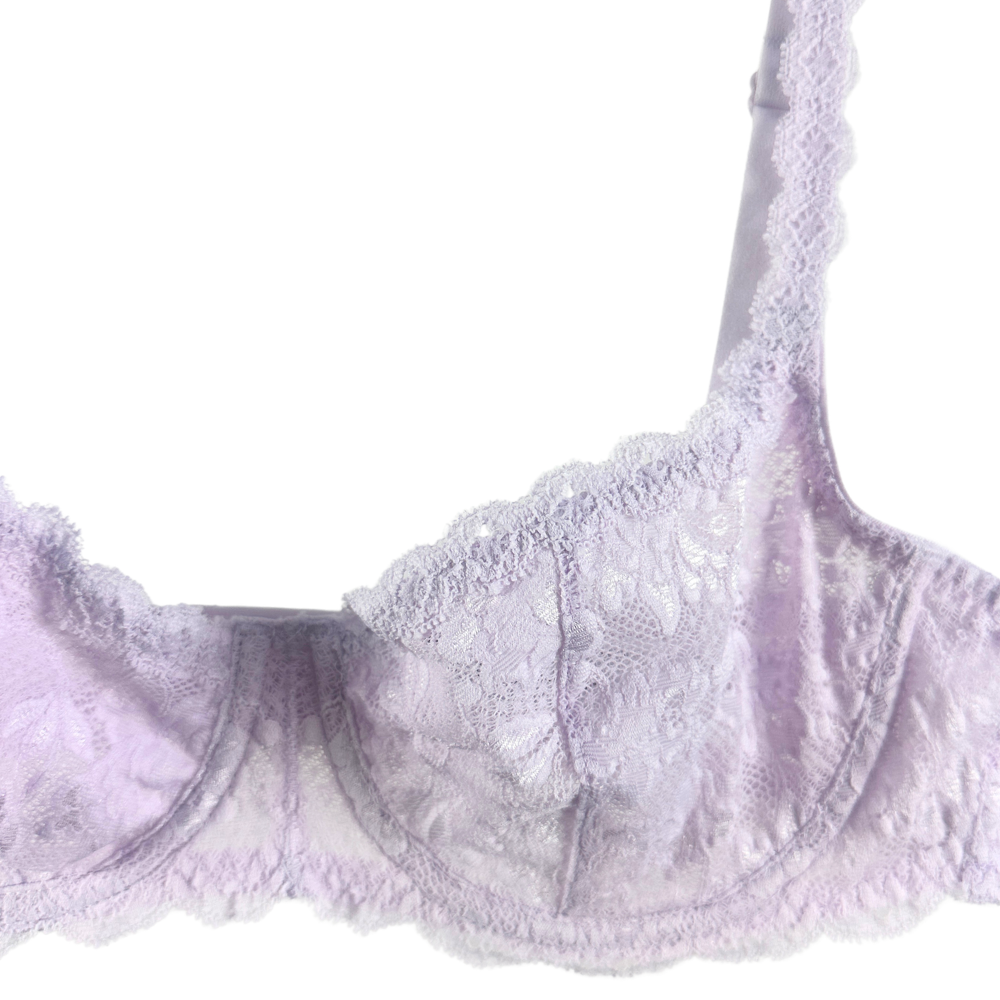 A close-up of a light lavender lace bra with scalloped edges and floral embroidered detailing, shown against a plain white background.