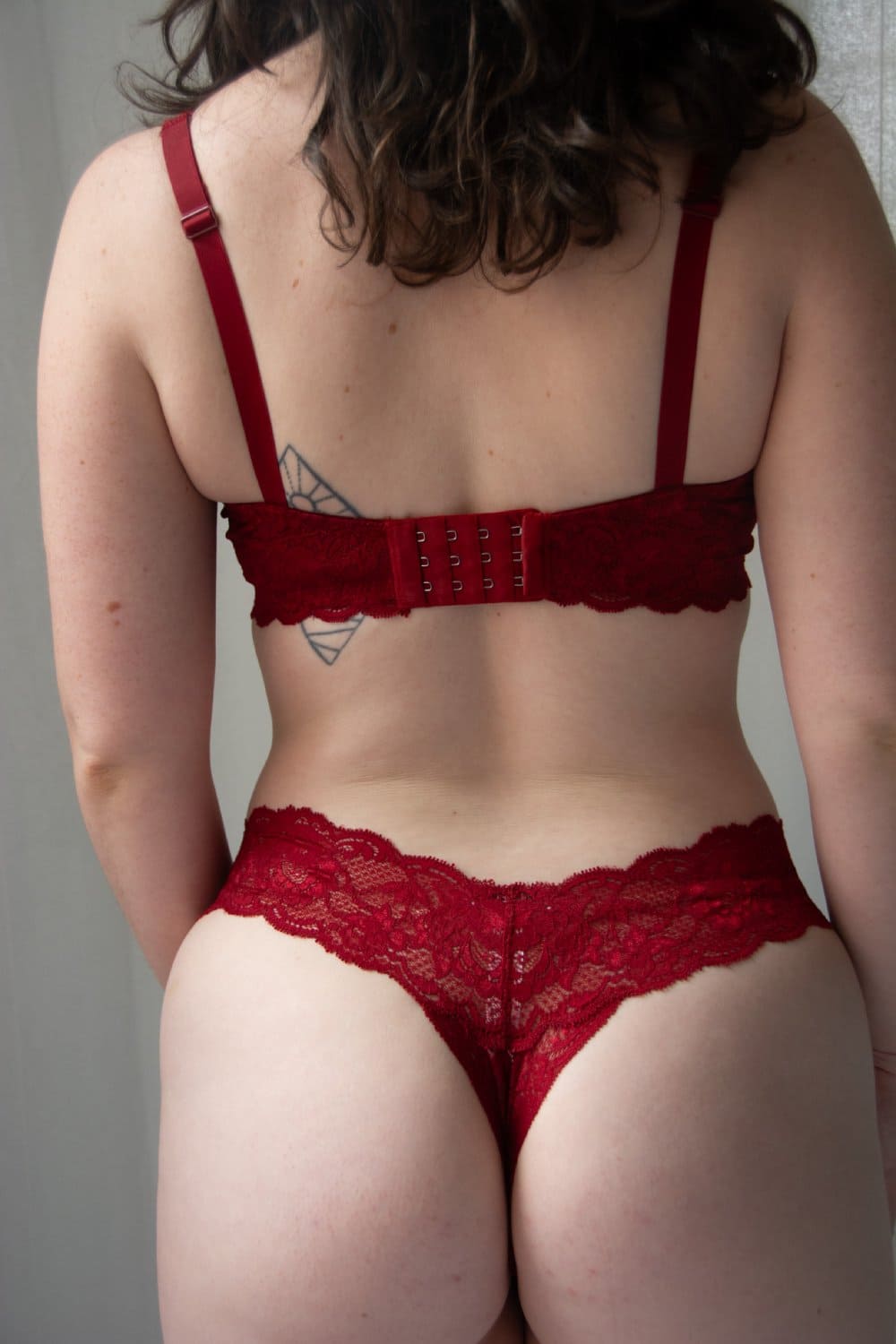Person wearing a red bra and underwear set against a neutral background
