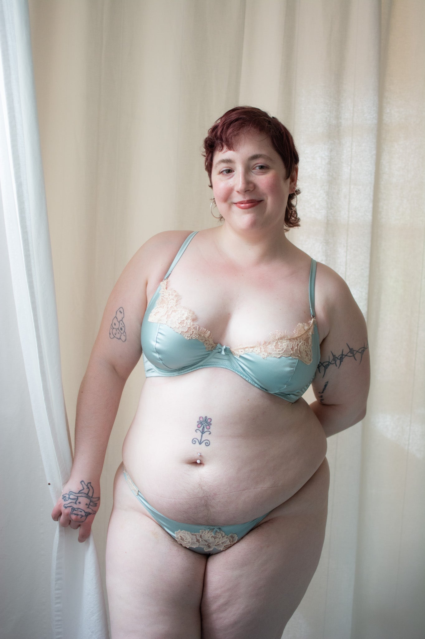 Person wearing a light blue bra and underwear set against a beige curtain background