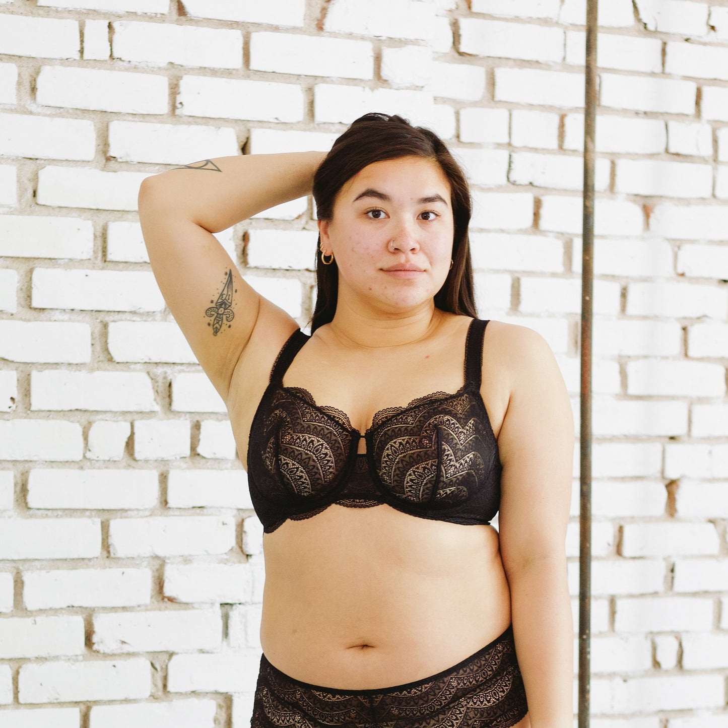 person wearing black lace lingerie set against a white brick wall