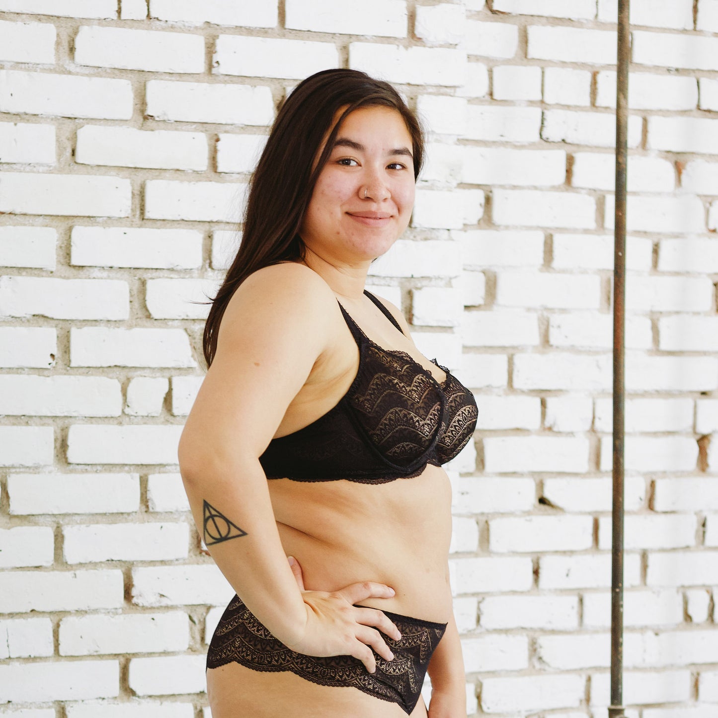 person wearing black lace lingerie set against a white brick wall