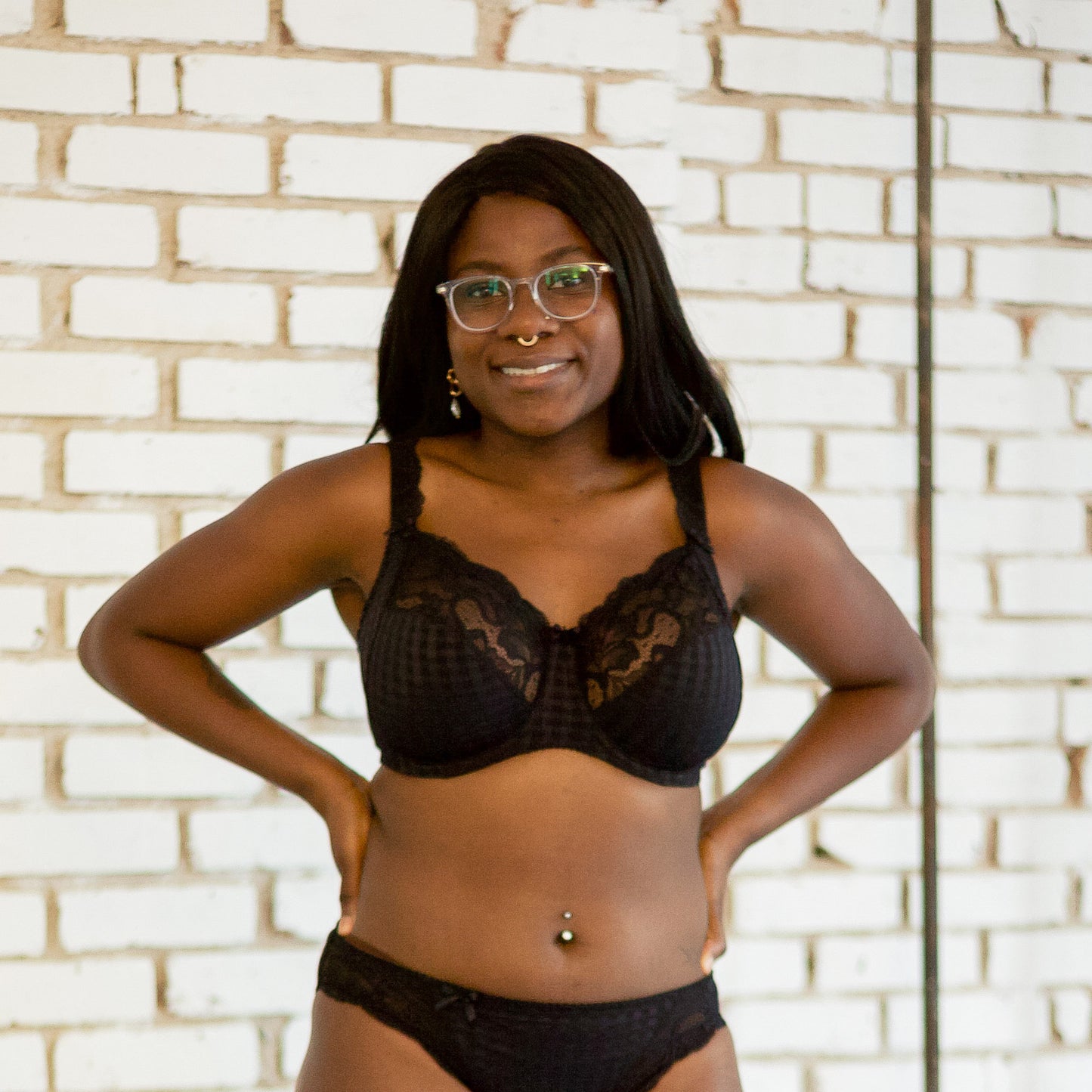 Model wearing black lace full cup bra and matching underwear in a sunlit room. 