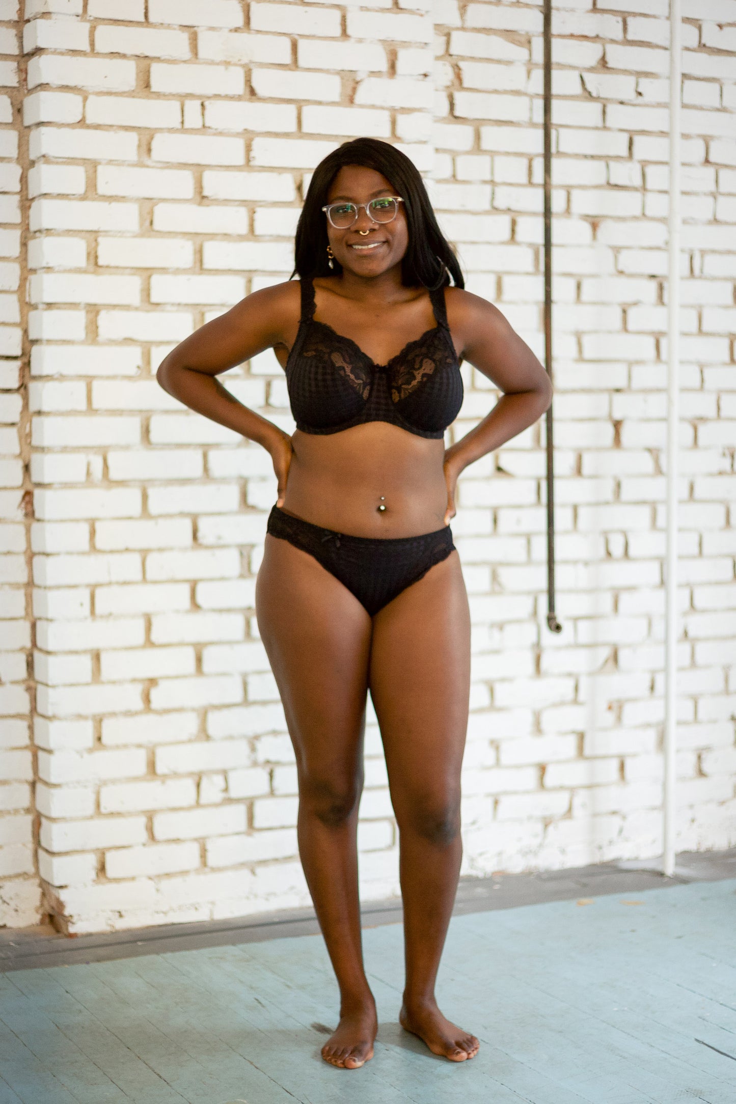 Model wearing black lace full cup bra and matching underwear in a sunlit room. 